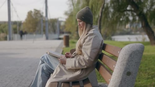 Woman Finds Solitude Reading on a Bench Near the Scenic Lake