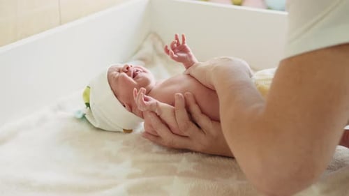 Adult Massaging Crying Newborn Baby on Changing Table