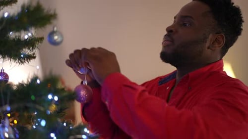 Man Decorates Christmas Tree with Festive Ornaments