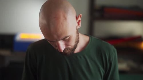 Close Up Front Shot of Man with Beard in Khaki Tshirt Looking Down and Sewing Handbag in Workshop