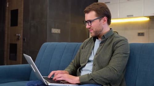 Man Works on Laptop at Home on Couch