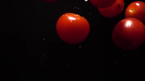 Tomates de cereja frescos caindo sobre um fundo preto em câmera lenta 100 quadros por segundo