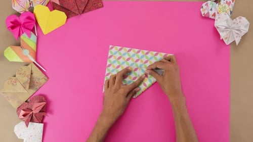 Hands Create Origami Heart on Pink Surface