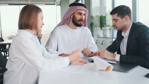 Mit einem Plan arbeiten. Muslimischer Geschäftsmann in traditioneller Kleidung mit Kollegen im Amt.