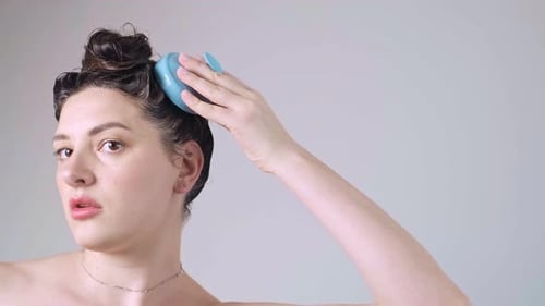 Close-up of the top of a head, hand holding a silicone head massager, performing a deep cleansing an