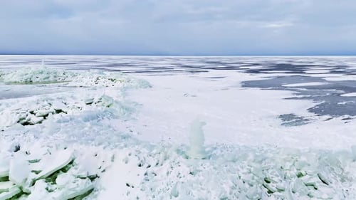 Wide drone view of frozen sea ice ridges with a small handmade ice tower, snow-covered surface, and