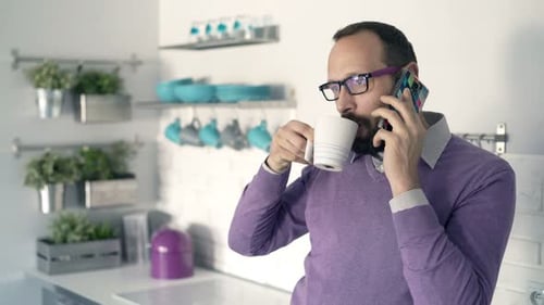 Man Talks on Phone and Drinks Coffee Indoors