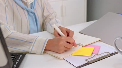 Close up of businesswoman taking notes and using laptop device in office.