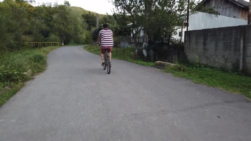 Nahaufnahme eines männlichen Radfahrers, der von hinten auf einer Landstraße gefilmt wurde. Mann in lässiger Sommerkleidung