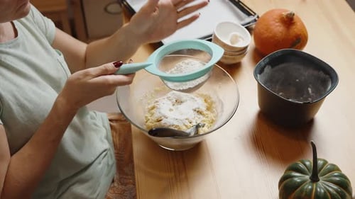 Homemade Pumpkin Cookie Recipe. Woman sifts flour, making the dough.