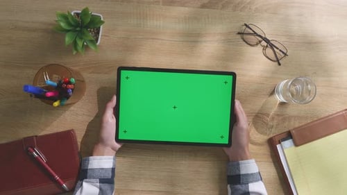Top down view of man's hands holding a mock up green screen tablet on a desk