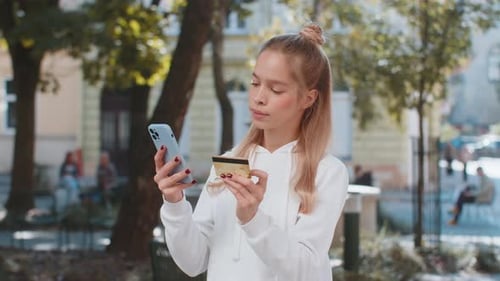 Happy Young Woman Using Credit Bank Card and Smartphone Purchases Online Shopping on City Street