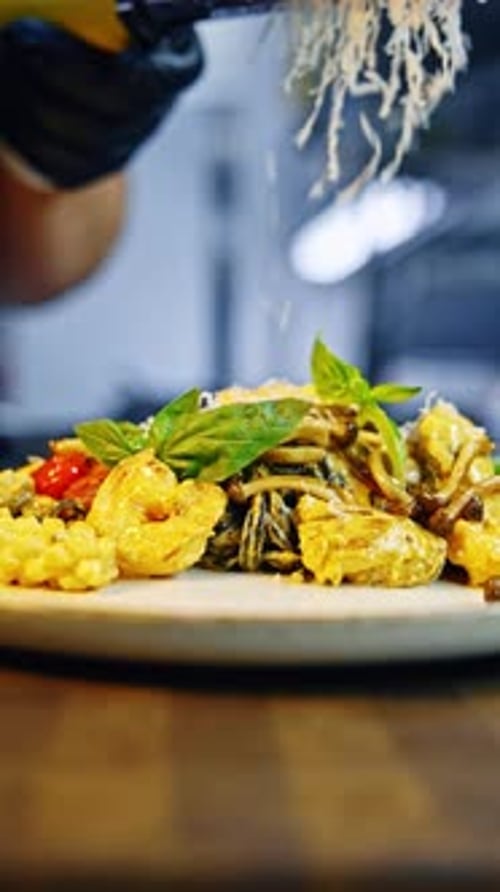 Cook in black gloves grates cheese on top of pasta. Serving spaghetti with sauce