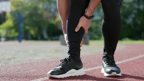 Close up; injured leg of a male athlete at the city stadium. Man massaging stretching, trauma injury
