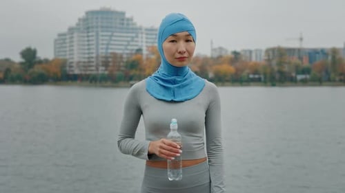 Woman in Head Covering by Lake with Water Bottle