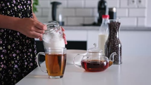 Woman Adding Sugar to Tea in Kitchen