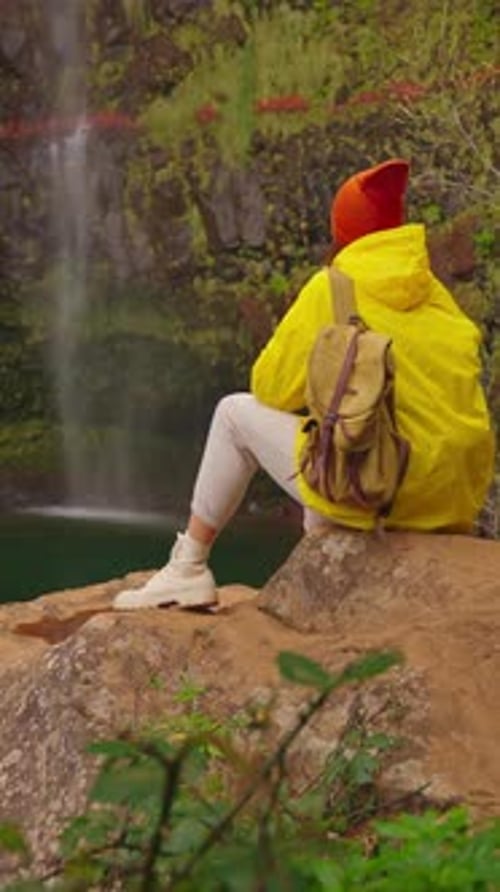 Vertical Video Woman Traveler Hiker in a Yellow Raincoat Near Waterfall in the Highlands Enjoys