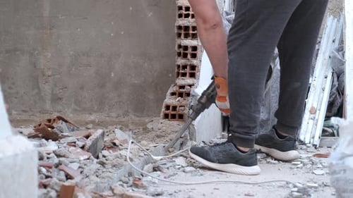 Unrecognizable man using a jackhammer to drill into wall.