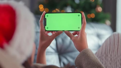 Woman holding mock up mobile smartphone with green screen or Chroma Key on background Christmas