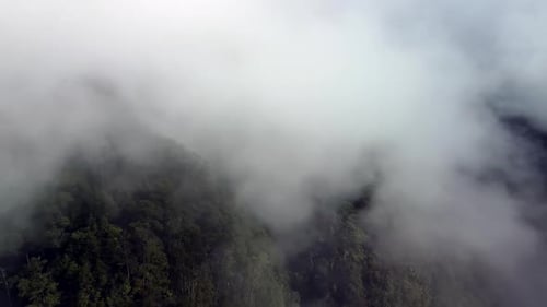 Aerial fly through clouds hanging over Tree covered Mountain.