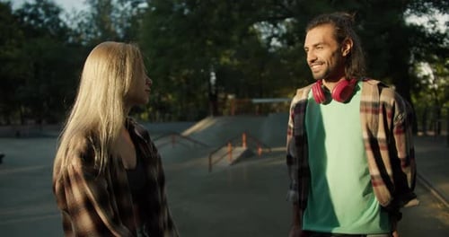 A Brunette Guy in a Green Tshirt Red Headphones in a Checkered Shirt Stands and Talks to a Blonde