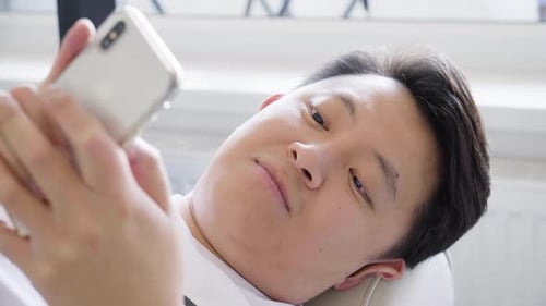 A Young Asian Man Works on a Smartphone As He Lies on a Couch Closeup