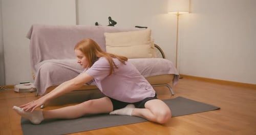 Redhaired Woman Performs Leg Stretches on Floor at Home