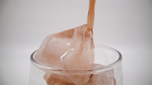 Pouring cola into a glass with ice close up isolated