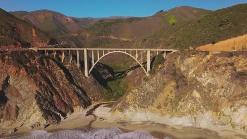 Arched bridge over the gap between the mountains. Sunlit mountains of California