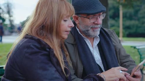 Mature Couple Using Smartphone Sitting on Bench in the Park