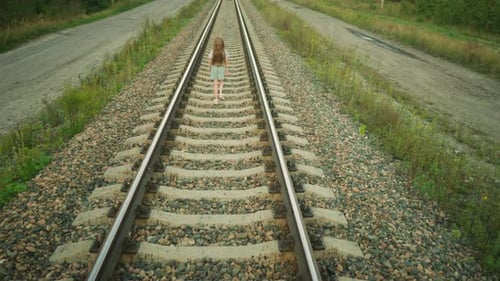 Rear View of Girl Walking on Rail Track in Rural Setting Holding Object