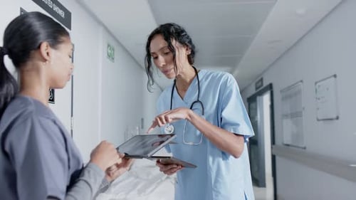 Diverse doctor and nurse using tablet and talking in corridor at hospital, in slow motion