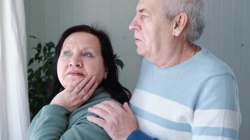 Concerned Senior Couple Looking Out Window Together
