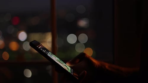 Hand Scrolling Through Content on Mobile Phone at Night