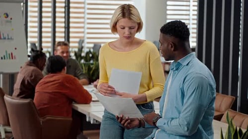 Confident Colleagues Discussing New Project in the Office Over Background of a Team at Meeting Table
