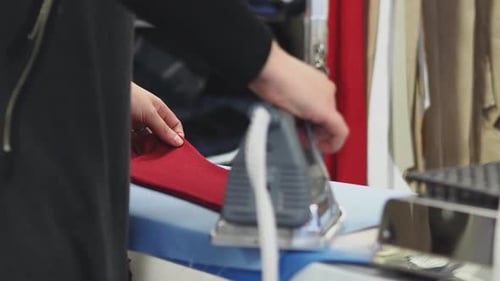 A woman ironing a red dress. It's an industrial iron made for professionals.