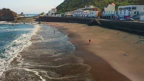 Ocean waves washing sandy volcanic beach at sunrise. Unrecognizable people enjoy vacation on seaside