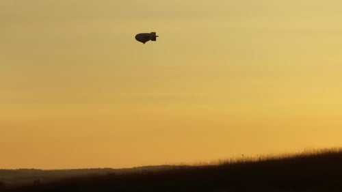 Silhueta de um dirigível viajante no céu durante o pôr do sol enquanto dirige em terra, portátil estático
