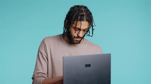 Man Inputting Data on Laptop While Standing in Blue Studio Background