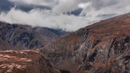 White clouds rushing over the mountain range, sun rays piercing through, lighting the barren tundra