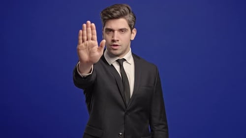 Man in Suit Gesturing Stop on Blue Background