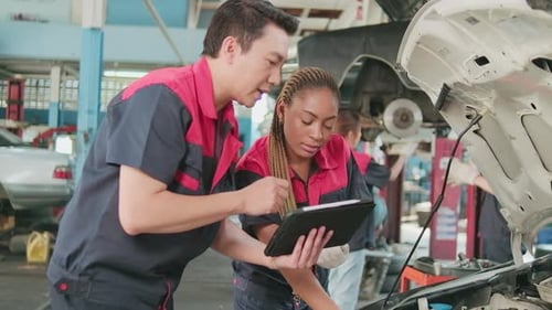 A male automotive supervisor and a Black female mechanic work in a car garage.