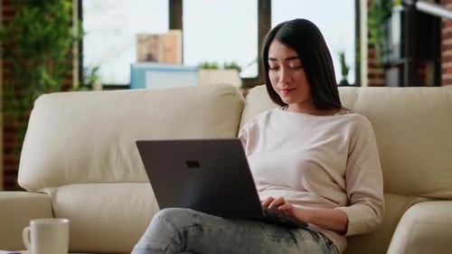 Smiling Office Worker at Home Working Remotely on Laptop While Sitting on Sofa in Living Room