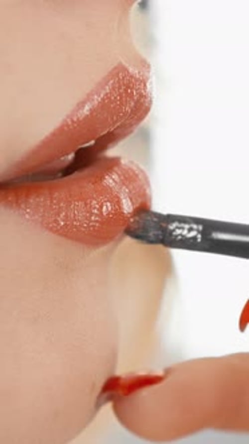 Vertikales Video, detaillierte Nahaufnahme, Frau trägt sorgfältig Lipgloss mit einem Pinsel auf, um ihre Schönheit zu unterstreichen