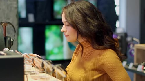 Attractive young girl with curly hair in an orange sweater chooses a smart watch in a store