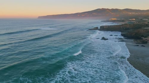 Amazing ocean waves rolling on coastal rocks at summer sunrise aerial view