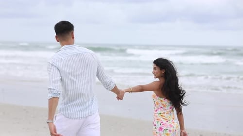 Romantic Young Couple Holding Hands Walking on the Beach
