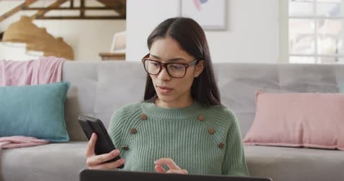Biracial woman using smartphone and working in living room