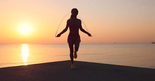 Fit woman jumping rope at the beach during summer vacation. Slow motion