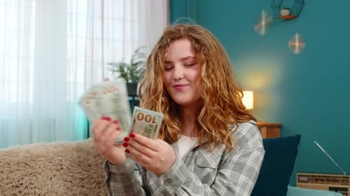 Woman Sits on Sofa Excitedly Counting Cash Dollars Celebrating Lottery Win or Unexpected Income Joy